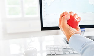 executive squeezes a stress ball in front of a computer displaying financial charts