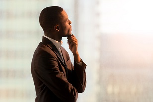 Portrait of pensive African-American businessman standing near window and thinking about decision