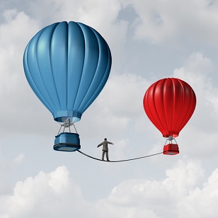 A business man walks a tight rope from a blue hot air balloon to a red one