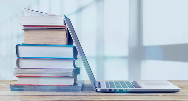 Laptop open with a stack of books piled up behind it. CUES Webinars are available for playback to all CUES members.
