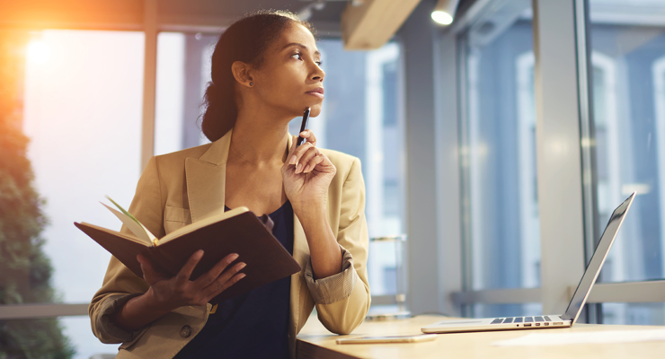 Business professional contemplating while looking at a notebook and computer