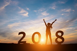 Silhouette of a woman in a victory pose in the position of the “1” in “2018,” in front of a sunset