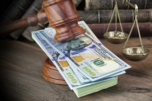 Wooden gavel resting on a stack of $100 bills in front of a set of brass scales, representating compensation and regulation
