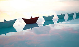 one red boat in a line of blue paper boats